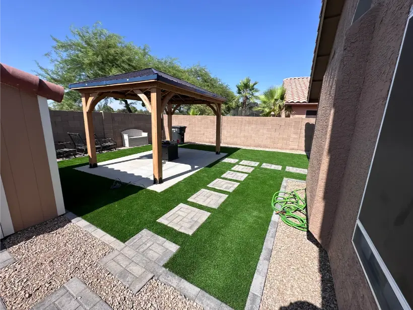Backyard with pergola, artificial grass, stepping stones, and patio furniture under clear blue sky.